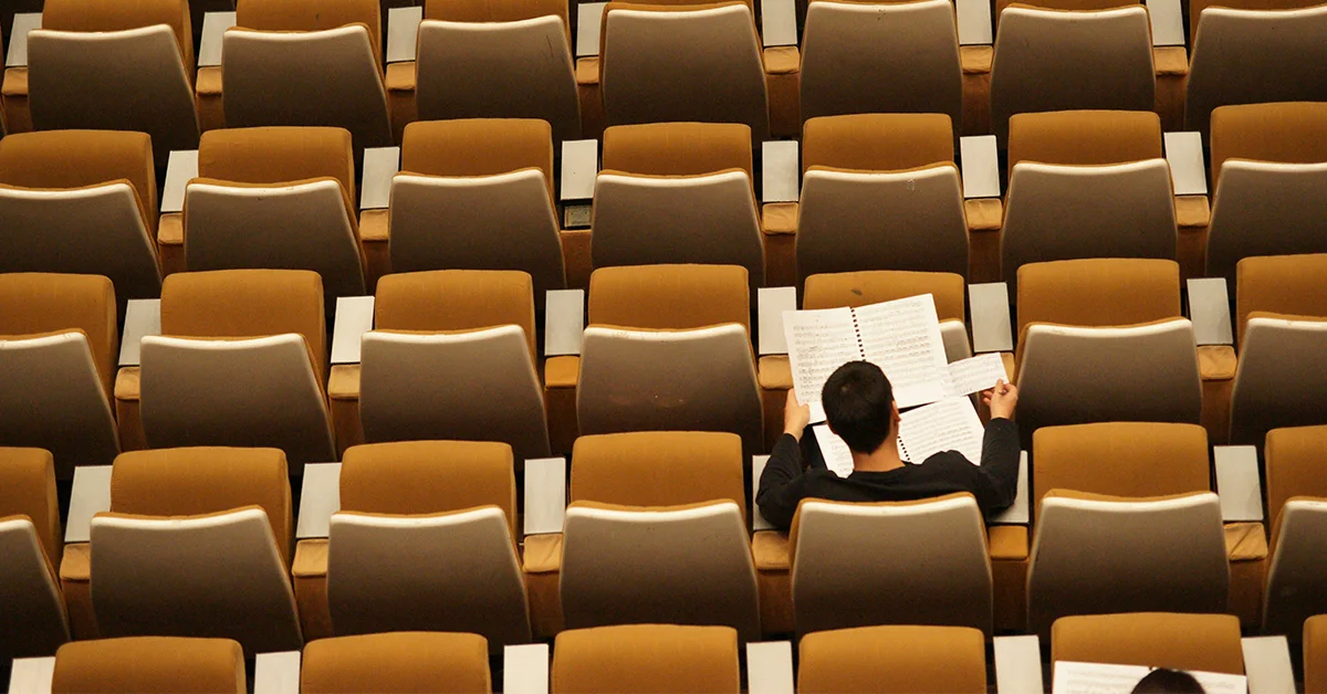 a student sitting along in an auditorium reviewing his sheet music (Navigating the College Enrollment Decline: Challenges and Opportunities for Higher Education article)