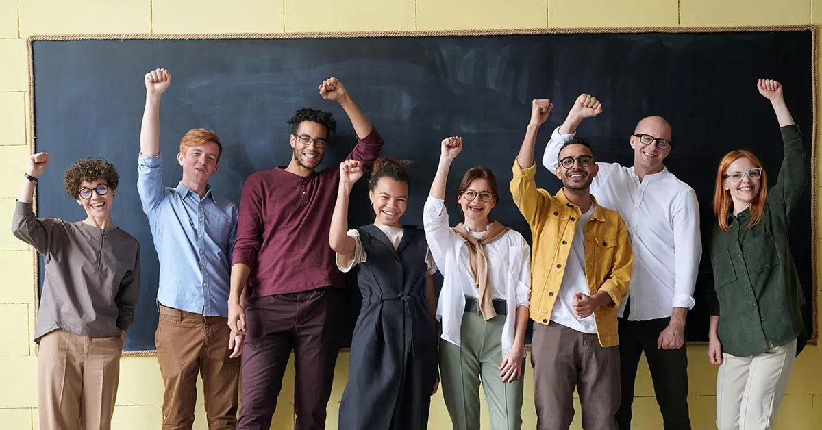 photo of a group of eight smiling teachers standing in front of a chalkboard with their hands raised victoriously (Rethinking the Learning Environment: Education Reform Now article)