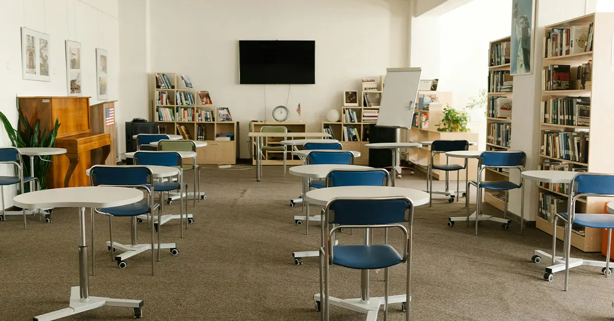 photo of an empty classroom with a piano against one wall, many bookshelves along the other walls, a whiteboard and monitor at the front, and wheeled desks (featured image: "Charter Schools vs Public Schools: A Comprehensive Guide for Parents" article)