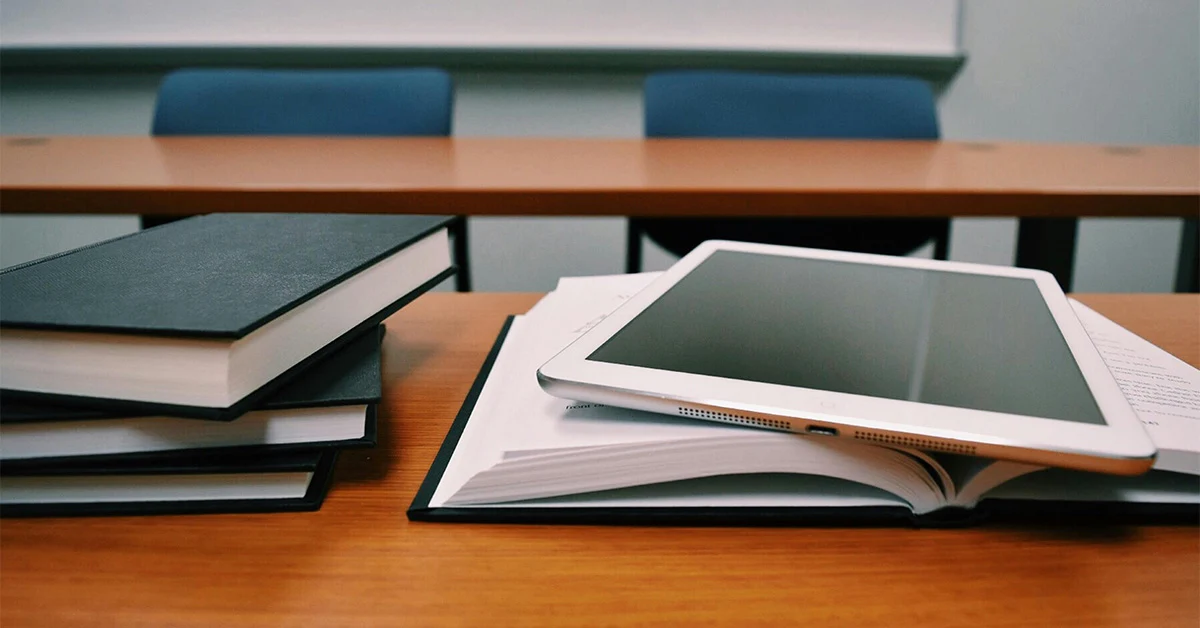 photo of a tablet sitting on an open book, a stack of closed books sits next to it (featured image: "Bridging the Digital Divide in Education" article)