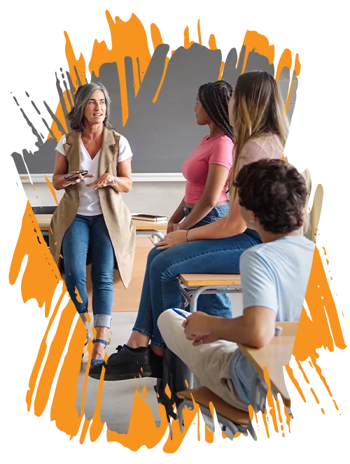 stylized photo of a female teacher leaning against her desk and talking to her high school students (About Education Revolution Association page - Our Vision)